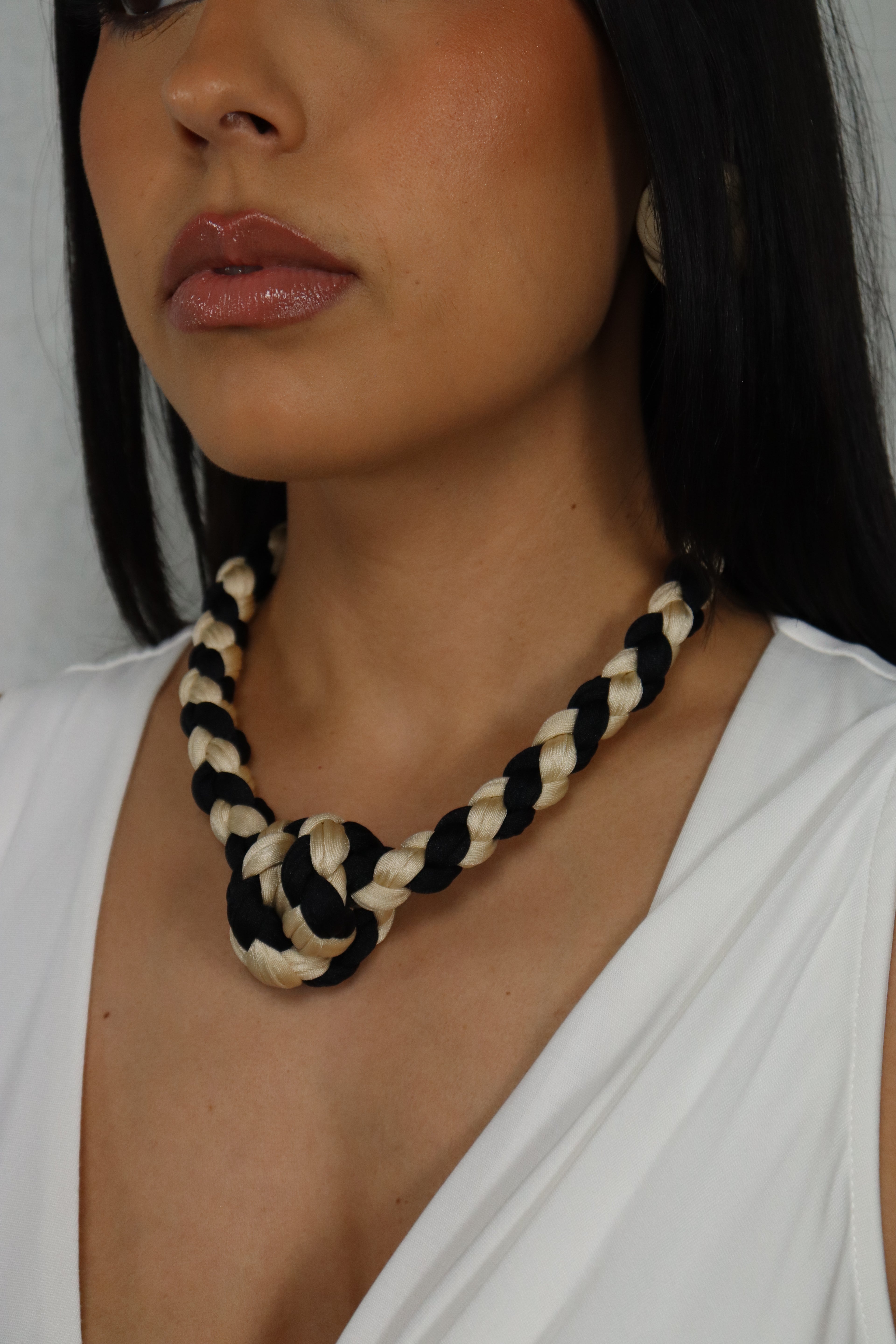 Person with a black and white rope around their neck, wearing a white top.