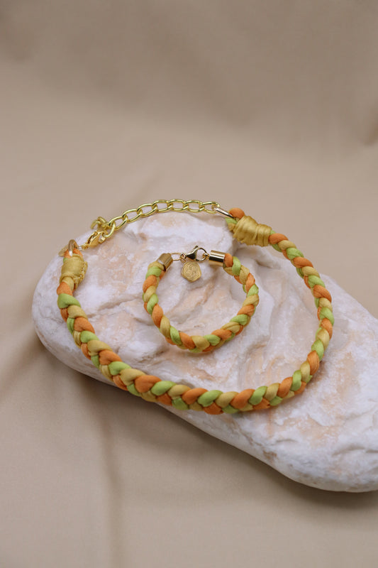 Braided bracelet and necklace with gold chain on a textured beige surface