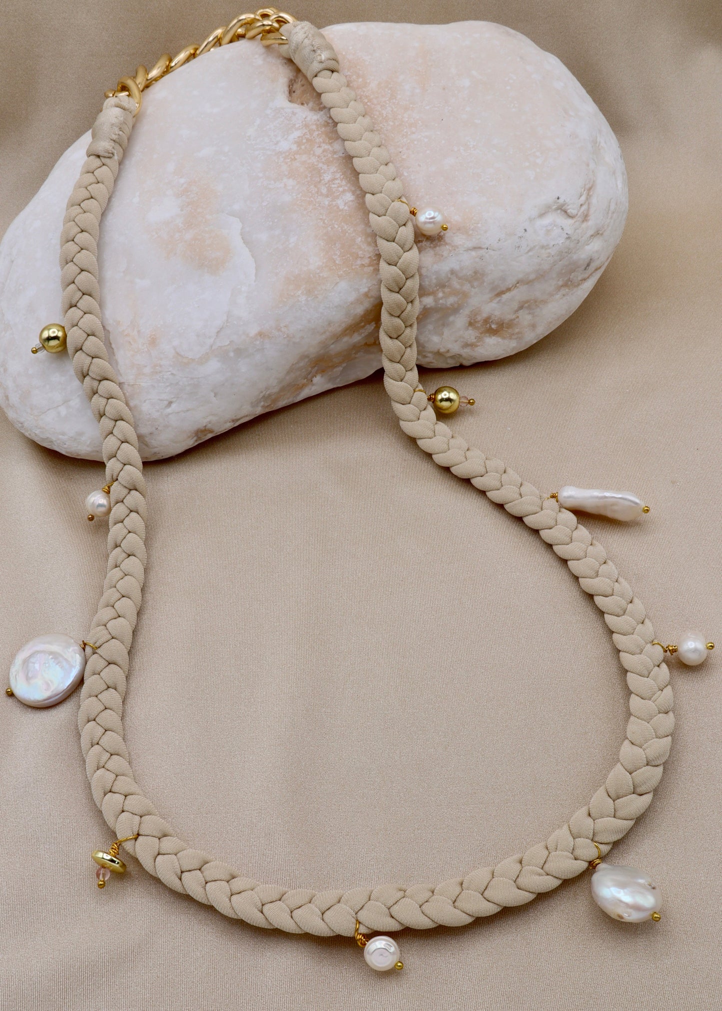 Braided necklace with pearls and gold accents on a beige surface
