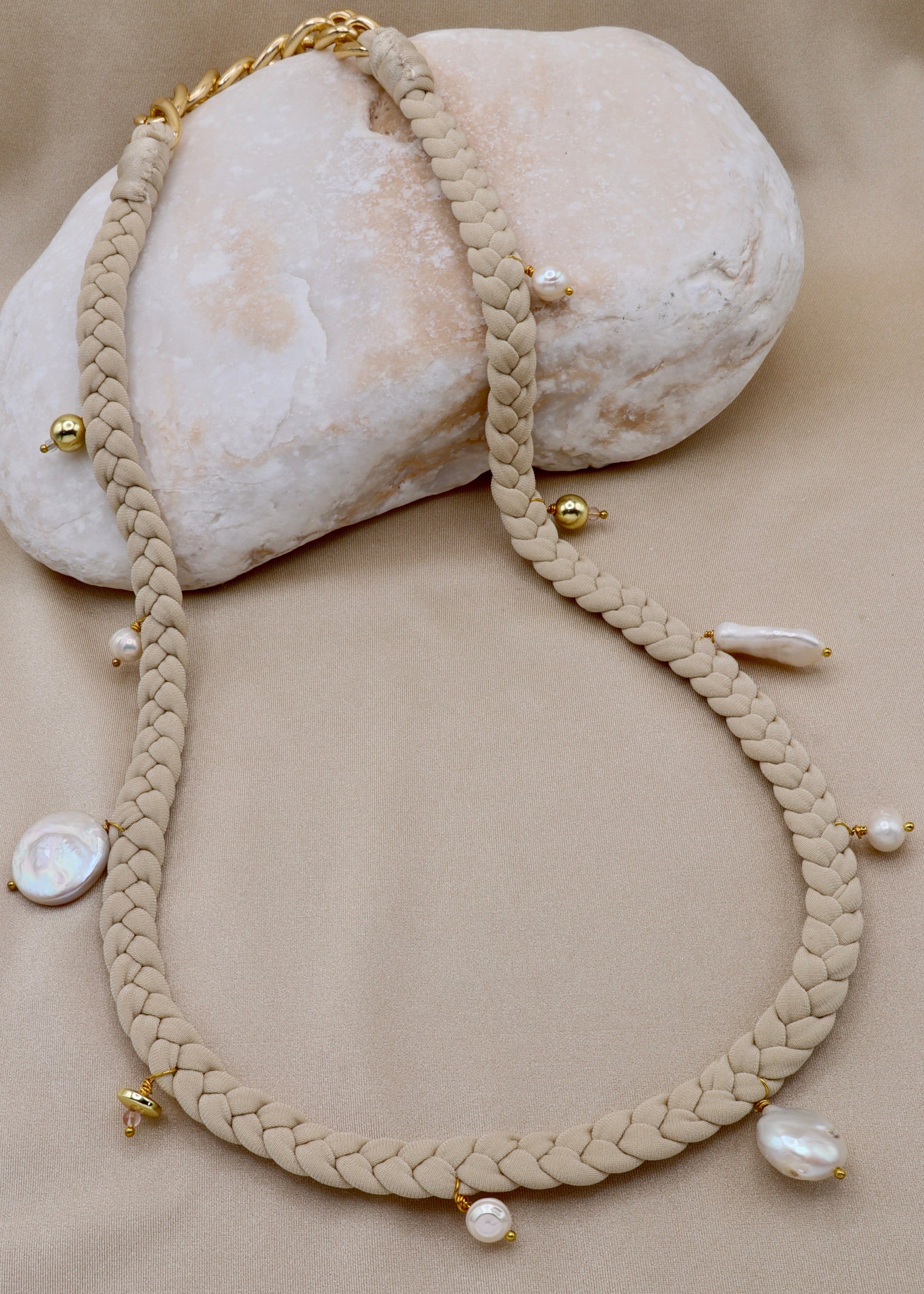 Braided necklace with pearls and gold accents on a beige surface